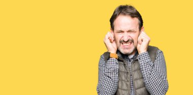 Orta yaş yakışıklı adam yüksek sesle müzik gürültü rahatsız ifade parmaklarıyla kulaklarıyla kapsayan kış yelek giyiyor. Sağır kavramı.