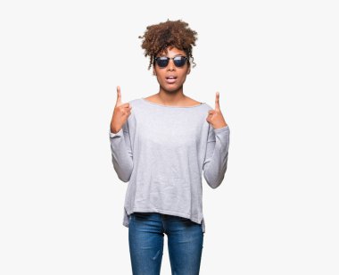 Güzel genç Afro-Amerikan kadın hayrete ve yukarıya bakıyor ve parmakları ile işaret ve silah kaldırdı sürpriz izole arka plan üzerinde güneş gözlüğü takıyor.