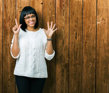 Güzel genç Afro-Amerikan kadın gözlük gösterilen ve parmakları ile işaret izole arka plan üzerinde kendinden emin ve mutlu gülümseyerek süre yedi numara.