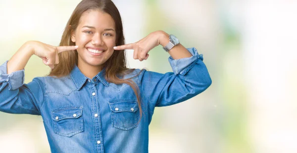 若い美しいブルネット女性の自信を示すと指歯と口を指して笑って孤立の背景に青いデニムのシャツを着てします 健康の概念 — ストック写真
