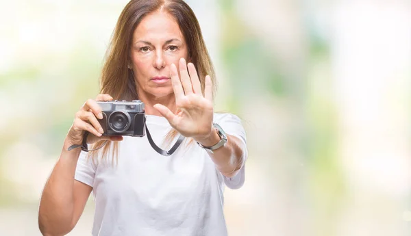中年西班牙裔妇女拍照使用老式照片相机在孤立的背景下 张开手做停止标志认真和自信的表达 防御姿态 — 图库照片