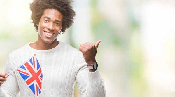 Afro american man flag of United Kingdom over isolated background pointing and showing with thumb up to the side with happy face smiling