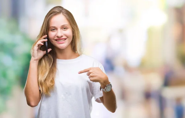 年轻美丽的金发碧眼的女人打电话使用智能手机在孤立的背景与惊喜的脸指向自己 — 图库照片