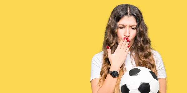 Young adult woman holding soccer football ball cover mouth with hand shocked with shame for mistake, expression of fear, scared in silence, secret concept