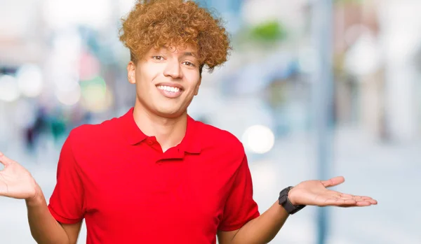 年轻的英俊男子与非洲头发红色 T恤微笑显示双手张开手掌 呈现和广告比较和平衡 — 图库照片