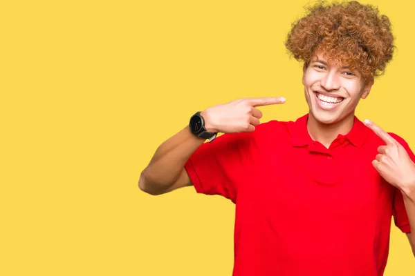 年轻英俊的男子与非洲头发红色 T恤微笑着显示和手指的牙齿和嘴指向 健康理念 — 图库照片