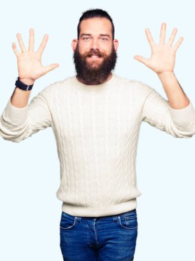 Kış kazak gösterme ve parmakları ile işaret giyen genç hipster adam kendinden emin ve mutlu gülümseyerek süre on numara.