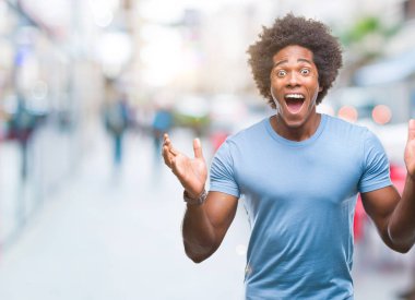 Afro Amerikalı adam deli kutluyor ve silah ile başarı için heyecanlı çığlık kaldırdı ve açık gözleri hayret izole arka plan üzerinde. Kazanan kavramı