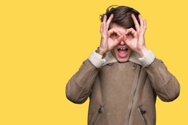 Yakışıklı delikanlı üzerinde kış palto giyiyor, dilini parmaklarının arasından baktığını yapışmasını dürbün gibi ok jest yapıyor arka plan izole. Deli ifade.