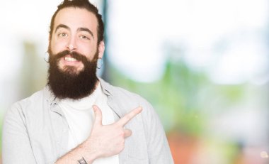 Uzun saç, sakal ve küpe neşeli bir gülümseme ile el ve parmak kadar yan yüzünde mutlu ve doğal ifade ile işaret yüz ile genç adam