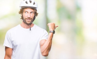 Seyir ve başparmak yanında yukarıyı mutlu yüz ile gülümseyen izole arka plan üzerinde güvenlik kask giymiş yakışıklı İspanyol bisikletçi adam.
