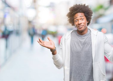 Afro Amerikalı adam izole arka plan clueless ve şaşkın bir ifadeyle kollar ve eller kaldırdı üzerine kazak giyiyor. Şüphe kavramı.