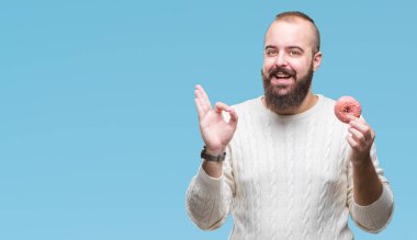 Genç beyaz hipster adam parmak, mükemmel sembolü ile ok işareti yapıyor izole arka plan üzerinde tatlı çörek yeme