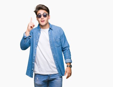 Genç yakışıklı adam başarılı fikirle izole arka plan işaret parmağı üzerinde güneş gözlüğü takıyor. Çıktıktan ve mutlu. Bir numara.