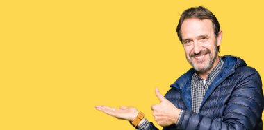 Kış palto gösteren palm el giyiyor ve yukarıya, mutlu ve neşeli gülümseyen baş parmakları Tamam jest yapıyor orta yaş yakışıklı adam