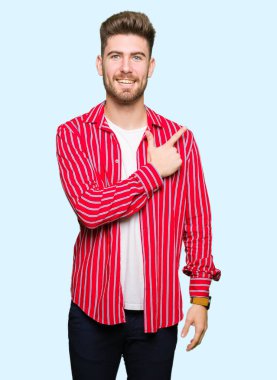 Genç yakışıklı giyen kırmızı gömlek neşeli bir gülümseme ile el ve parmak kadar yan yüzünde mutlu ve doğal ifade ile işaret yüz adam