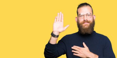 Gözlük ve balıkçı yaka kazak giyen genç sarışın adam göğüs ve bir sadakat sözü yemin yapma avuç, el ile küfür