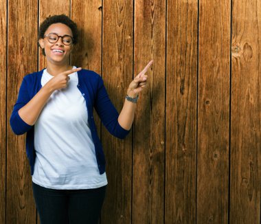 Genç güzel Afrikalı-Amerikalı kadın gülümseyerek ve iki elleri ve parmakları ile tarafına işaret kamera bakarak izole arka plan üzerinde gözlük.