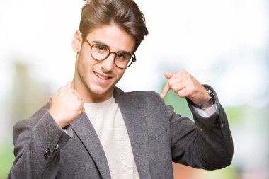 Yüzünde gülümseme ile kendinden emin görünüyorsun, kendini gururlu ve mutlu parmakları ile işaret izole arka plan üzerinde gözlük takan genç iş adamı.