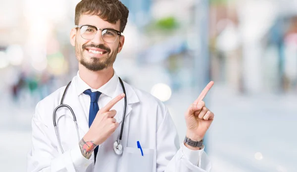 若い医者分離背景笑顔で側に つの手と指で指しているカメラ目線の上病院コートを着た男 — ストック写真