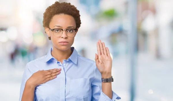 Young beautiful african american business woman over isolated background Swearing with hand on chest and open palm, making a loyalty promise oath