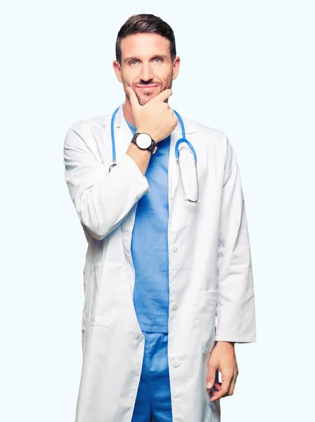 帅气的医生穿着医疗制服 穿着孤立的背景 在镜头前显得很自信 双臂交叉 双手举在下巴上 积极的思考 — 图库照片