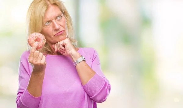 中年の金髪女性に関する質問は 非常に混乱して考え分離背景深刻な顔を考えての上ピンクのドーナツを食べる — ストック写真