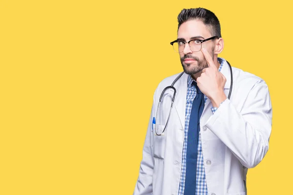 Handsome young doctor man over isolated background Pointing to the eye watching you gesture, suspicious expression