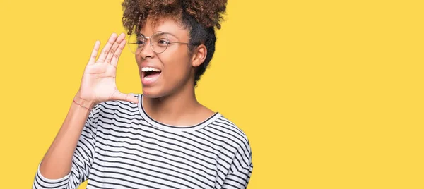 Beautiful young african american woman wearing glasses over isolated background shouting and screaming loud to side with hand on mouth. Communication concept.