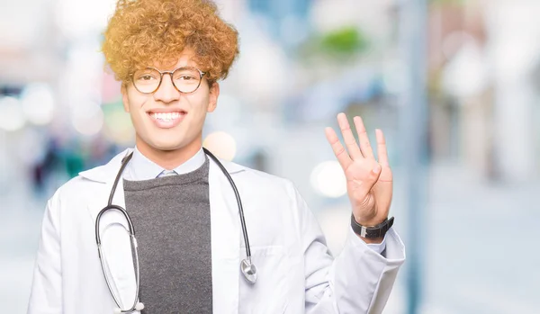 年轻英俊的医生男子穿着医疗外套显示和手指指向第四 而微笑着自信和快乐 — 图库照片