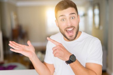 Casual beyaz t-shirt evde hayran giyen ve el ile sunulması ve parmak ile işaret ederken kameraya gülümseyen genç yakışıklı adam.