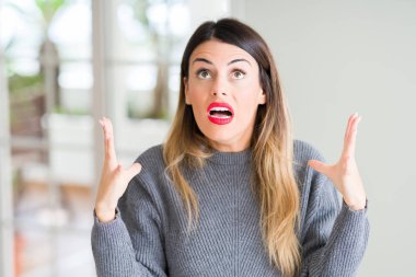 Evde çılgın ve kızgın bağırarak ve agresif ifade ve silah kaldırdı bağırmaya kış kazak giyen genç güzel kadın. Hayal kırıklığı kavramı.