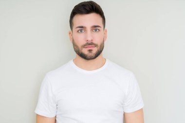 Genç yakışıklı giyiyor rahat beyaz t-shirt yüzünde ciddi bir ifade ile izole arka plan üzerinde adam. Basit ve doğal kameraya bakıyor.