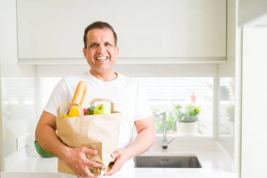 Orta yaş erkek holding grocieries evde sebze dolu çanta