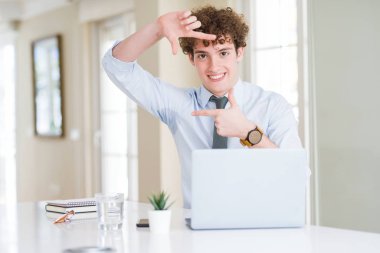 Genç iş adamı elle yapma çerçeve ve parmakları ile mutlu yüz gülümseyen ofiste bilgisayar laptop ile çalışma. Yaratıcılık ve Fotoğrafçılık kavramı.