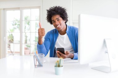 Çalışan Afrikalı-Amerikalı adam akıllı telefon ve bilgisayar mutlu ok işareti yapıyor büyük gülümseme ile kullanarak başparmak yukarı parmaklarıyla, mükemmel işareti