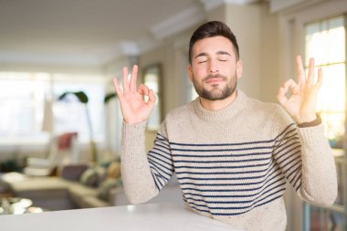 Genç yakışıklı adam evde dinlenin ve gülümseyen gözlerle parmak ile meditasyon jest yapıyor kapalı. Yoga kavramı.