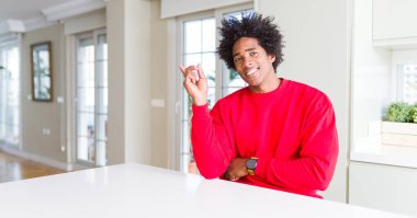 Afrika kökenli Amerikalı adam yüzünde, kocaman bir gülümseme ile rahat kırmızı kazak giyen kameraya bakarak yan el ve parmak ile işaret.