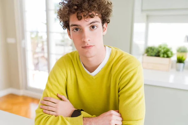 年轻英俊的男人穿着黄色毛衣在家里放松与严肃的表情在脸上 简单和自然与交叉的武器 — 图库照片