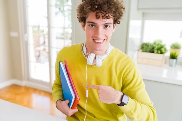 ヘッドフォンを身に着けているとノートブックを手と指で指している非常に満足して保持している若い学生男 — ストック写真
