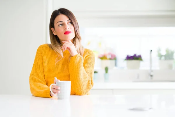 Young beautiful woman drinking a cup of coffee at home serious face thinking about question, very confused idea