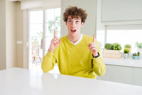 黄色いセーターを着て家で若いハンサムな男はびっくりし 驚き見て 指で指して 腕を上げた — ストック写真
