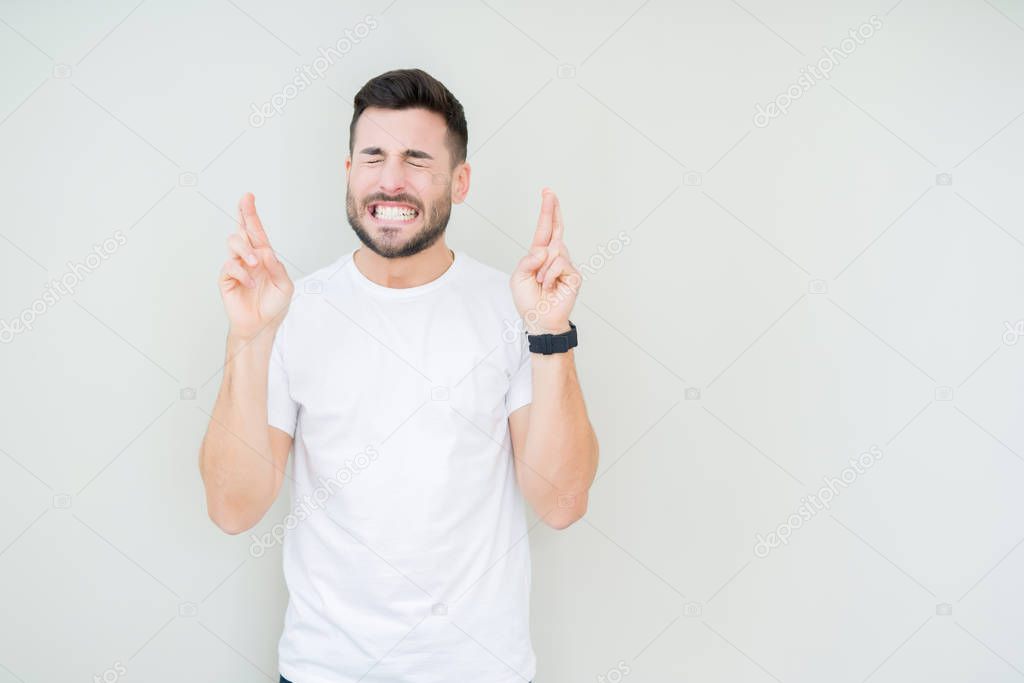 Young handsome man wearing casual white t-shirt over isolated background smiling crossing fingers with hope and eyes closed. Luck and superstitious concept.