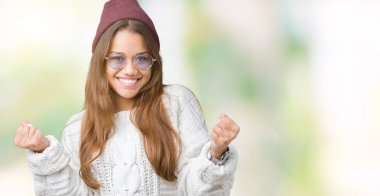 Güneş gözlüğü izole arka plan kutlama üzerinde giyen genç güzel esmer hipster kadın şaşırttı ve başarı için kaldırdı kollarını açarak hayret ve gözleri açık. Kazanan kavramı.