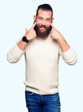 Kış kazak giyen genç hipster adam açık ağız ile gülümseyen, işaret ve neşeli zorla parmak gülümse