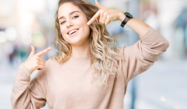 Sweatershirt kendine güvenen gösterilen ve işaret parmakları diş ve ağız ile gülümseyen izole arka plan üzerinde giyen güzel genç sarışın kadın. Sağlık kavramı.