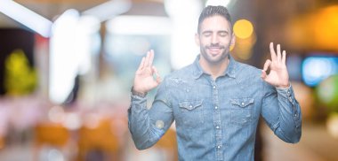 Yakışıklı delikanlı izole arka plan üzerinde dinlenmek ve gülümseyen gözlerle parmak ile meditasyon jest yapıyor kapalı. Yoga kavramı.