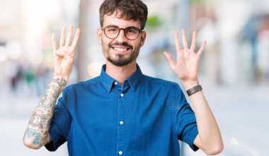 Gösterilen arka plan üzerinde gözlük takan genç yakışıklı adam izole ve parmakları ile işaret numara 9 kendinden emin ve mutlu gülümseyerek süre.