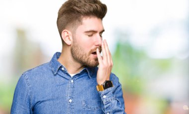 Genç yakışıklı sarışın adam rahat kot gömlek giymiş el ağzıyla kapsayan yorgun esneme sıkılmış. Restless ve uyku hali.