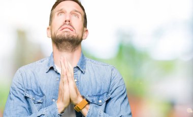 Denim ceket yalvarıyor ve umut ifade yüzünde çok duygusal ve endişe ile birlikte elleriyle dua sakal ve mavi gözlü yakışıklı adam. Bağışlanmak. Din kavramı.